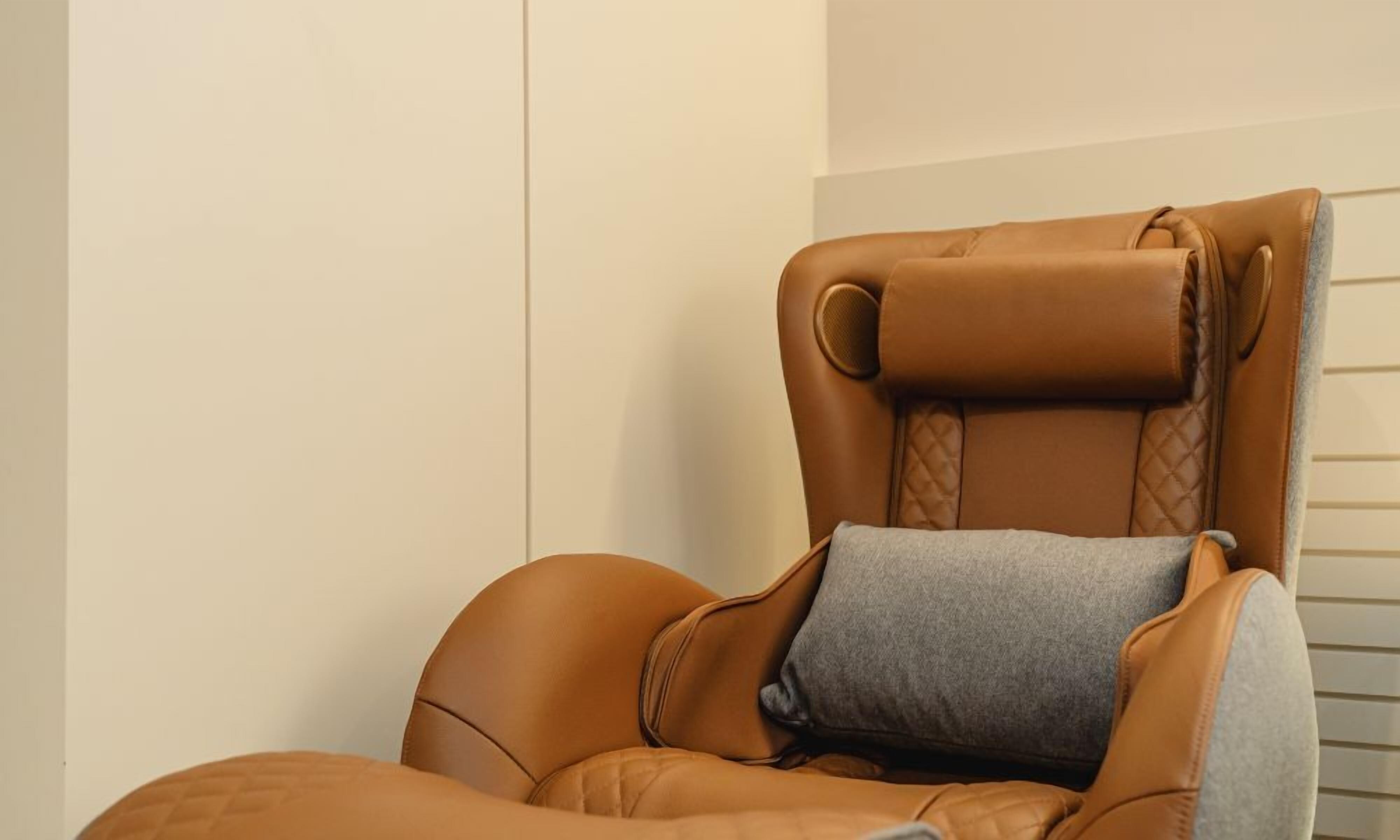 A tan leather massage chair with a headrest and a small gray pillow.
