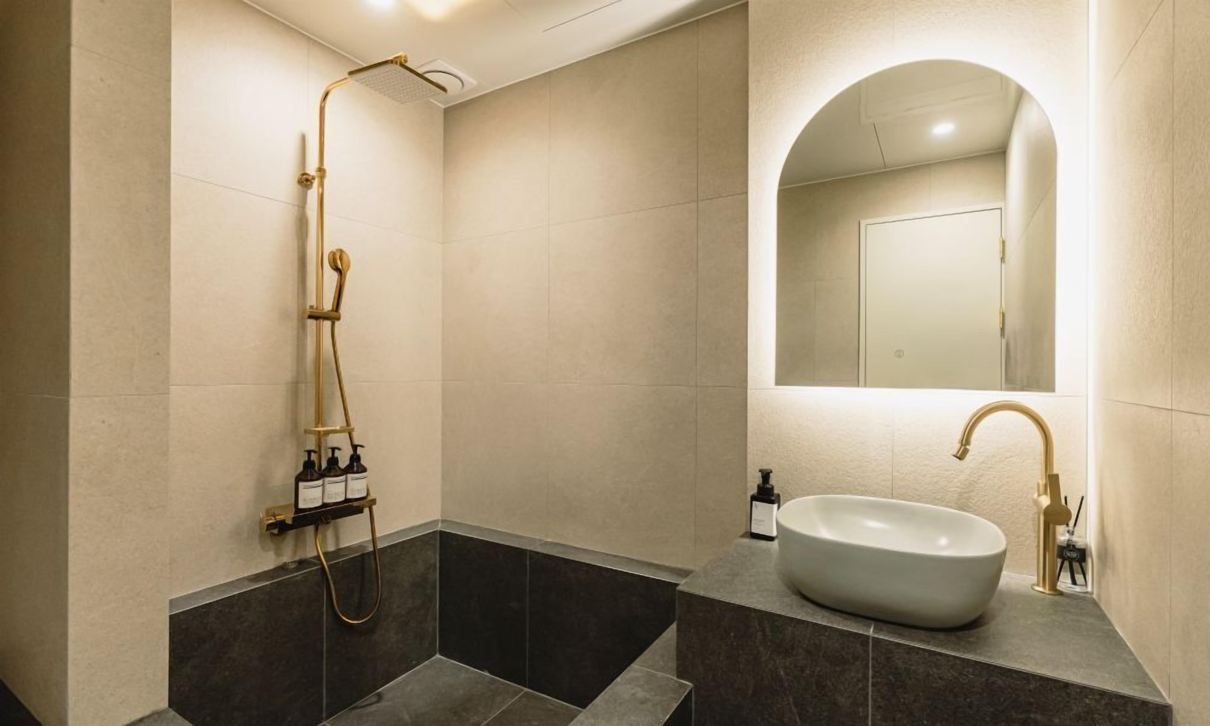 A modern bathroom with a freestanding bathtub, a large mirror, and a sink with a gold faucet.