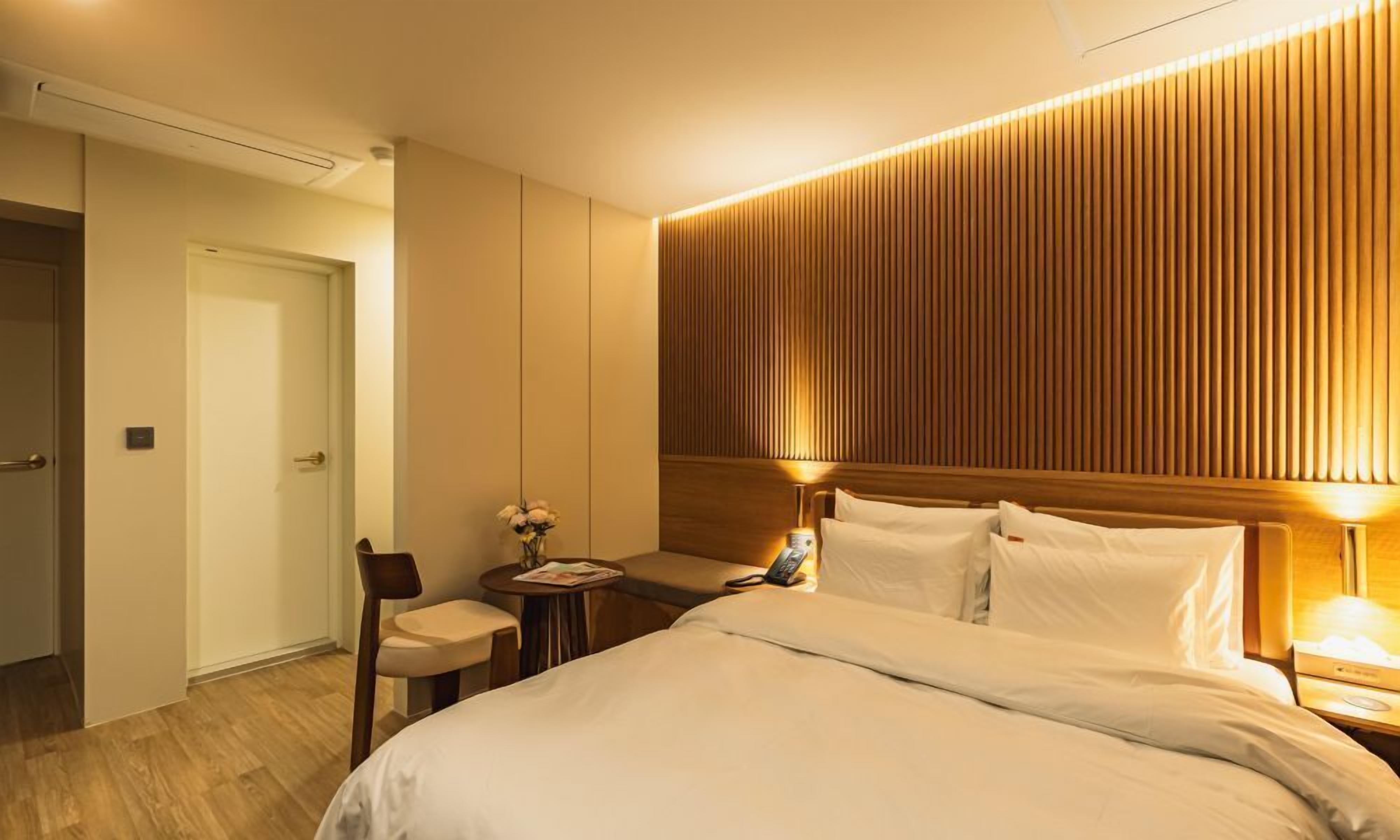 A hotel room with a large bed, bedside tables, a chair, and a wooden panel wall.