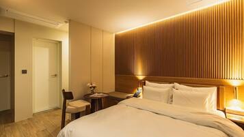 A hotel room with a large bed, bedside tables, a chair, and a wooden panel wall.