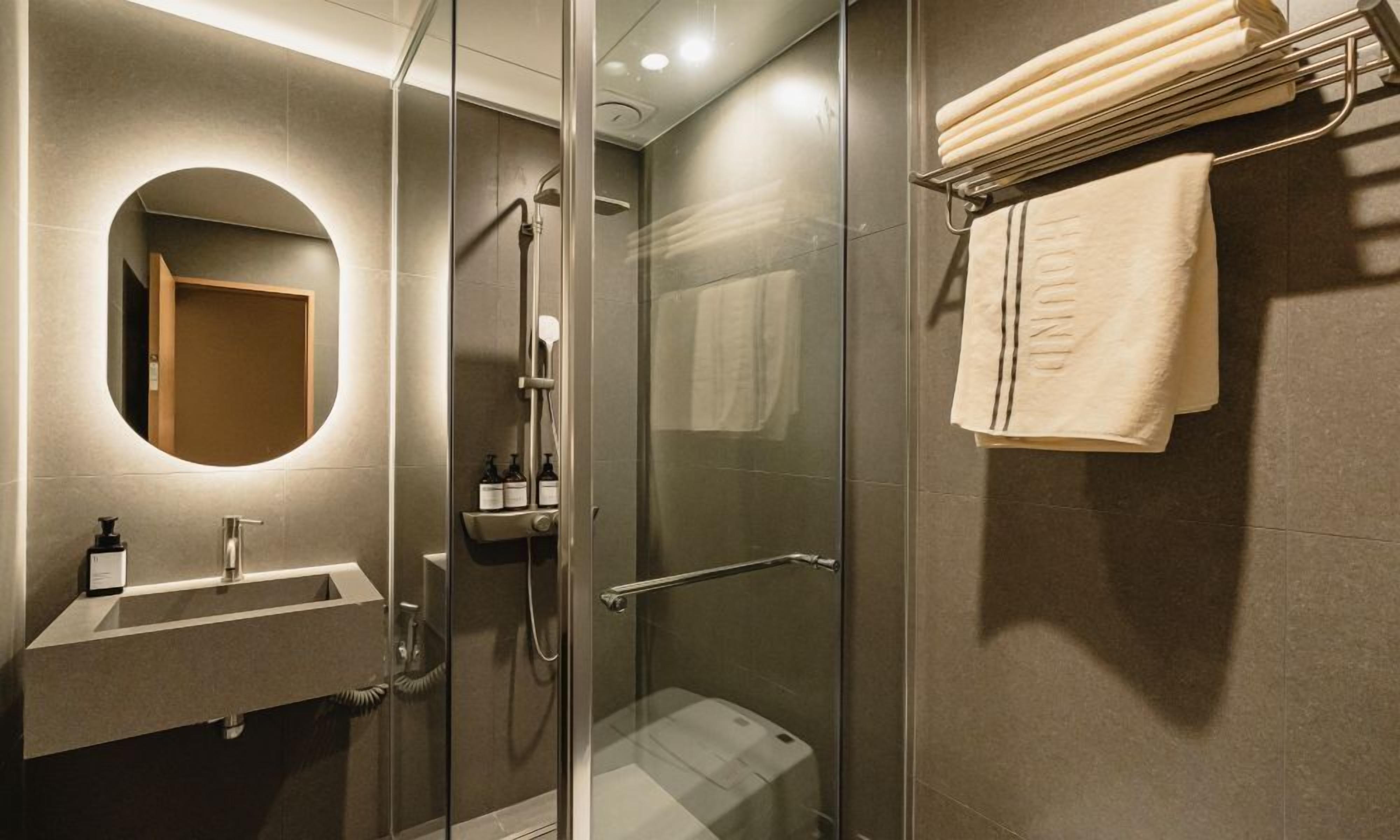 Un baño moderno con ducha de mampara de vidrio, un lavamanos con espejo y un perchero con toallas dobladas.