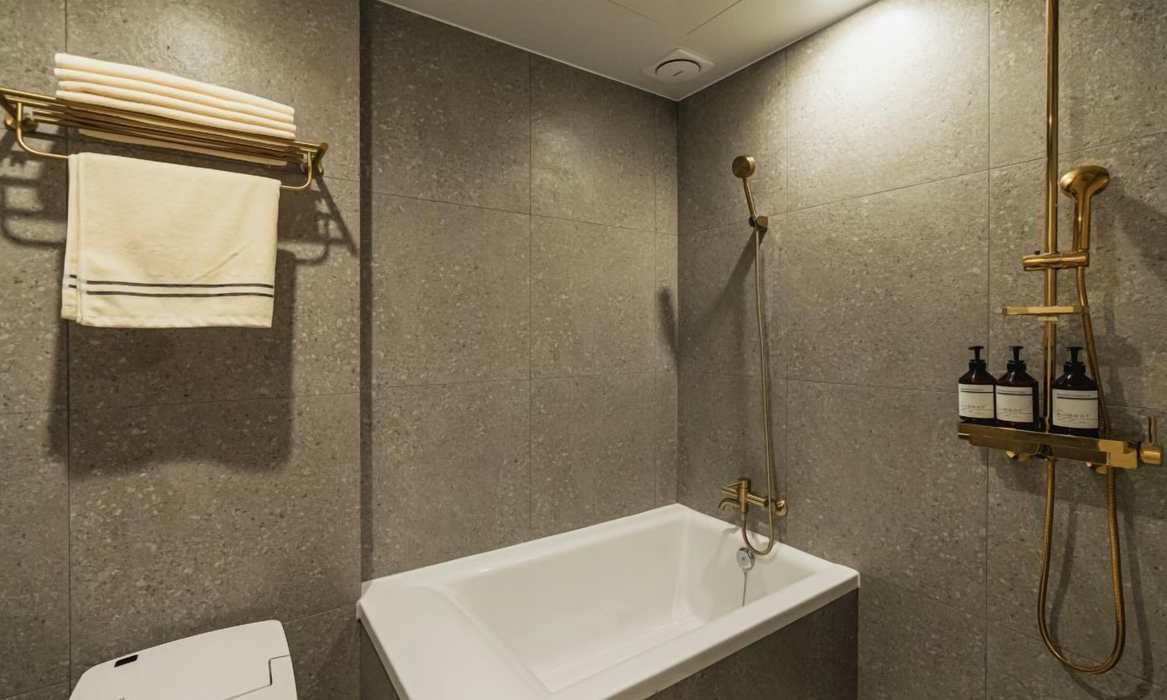 A bathroom with a white bathtub, a towel rack with folded towels, and a shower with a gold fixture and bottles of shampoo.