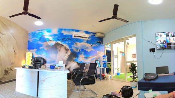Une salle dotée d’un comptoir d’accueil en marbre, d’une grande fresque représentant des nuages et un visage, de ventilateurs de plafond et d’un téléviseur mural.