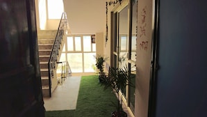 Un couloir avec un escalier, une moquette verte synthétique, des plantes en pot et une porte ornée de caractères chinois.