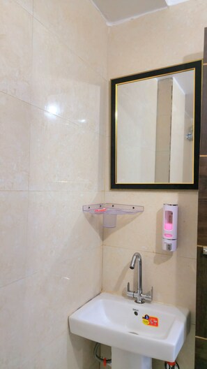 Een badkamer met een witte wastafel, een spiegel met gouden lijst en een zeepdispenser.