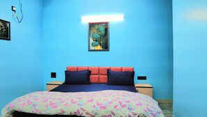 Une pièce avec un mur bleu, un lit recouvert d’une courtepointe à motifs floraux colorés, une œuvre d’art encadrée au-dessus du lit et une table de chevet avec une lampe.