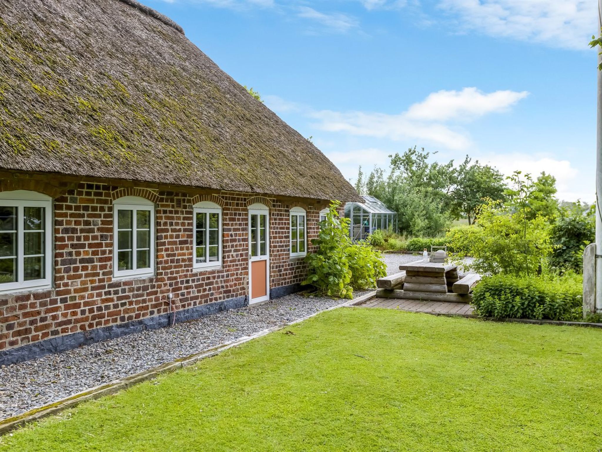 A traditional brick house with a thatched roof, a small garden, and a greenhouse.