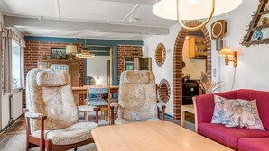 A cozy living room with a wooden table, two patterned armchairs, a red sofa, and a brick wall with decorative mirrors.