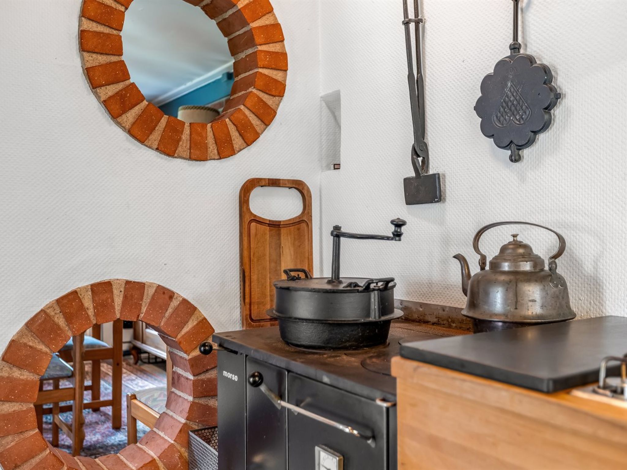 A rustic kitchen with a brick oven, a stove, a kettle, and a wooden cutting board.