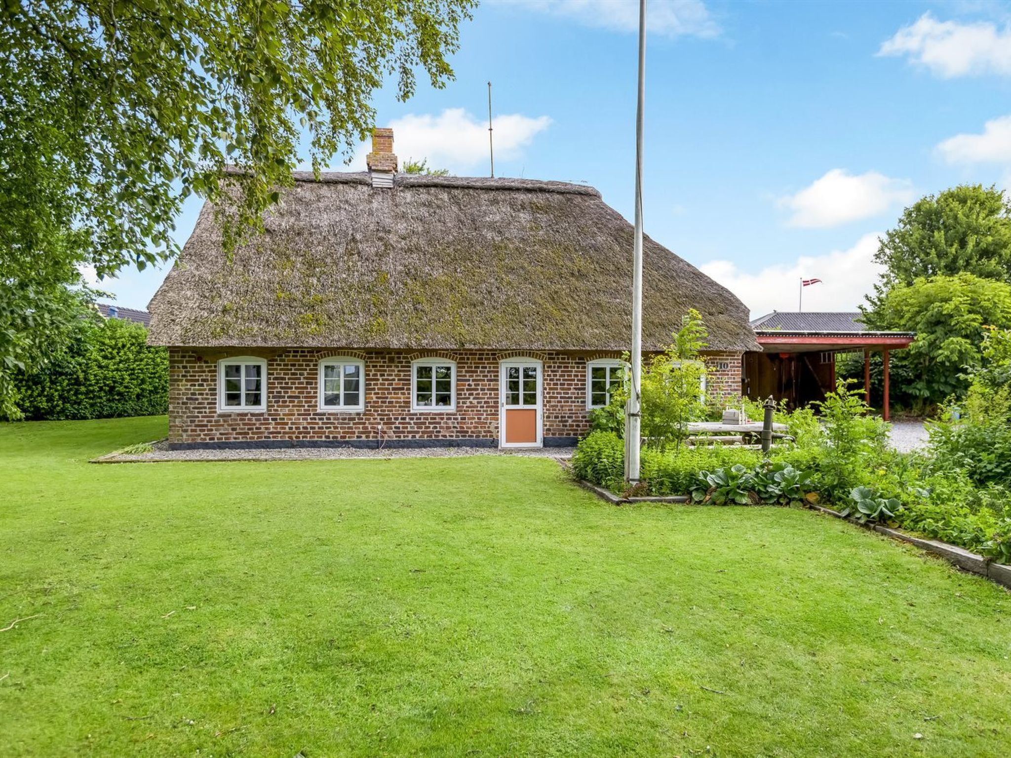A traditional brick house with a thatched roof, a well-maintained lawn, and a small garden area.