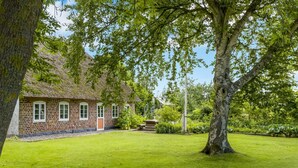A brick house with a thatched roof, surrounded by a well-maintained lawn and trees.