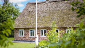 A thatched-roof house with brick walls and white-framed windows.
