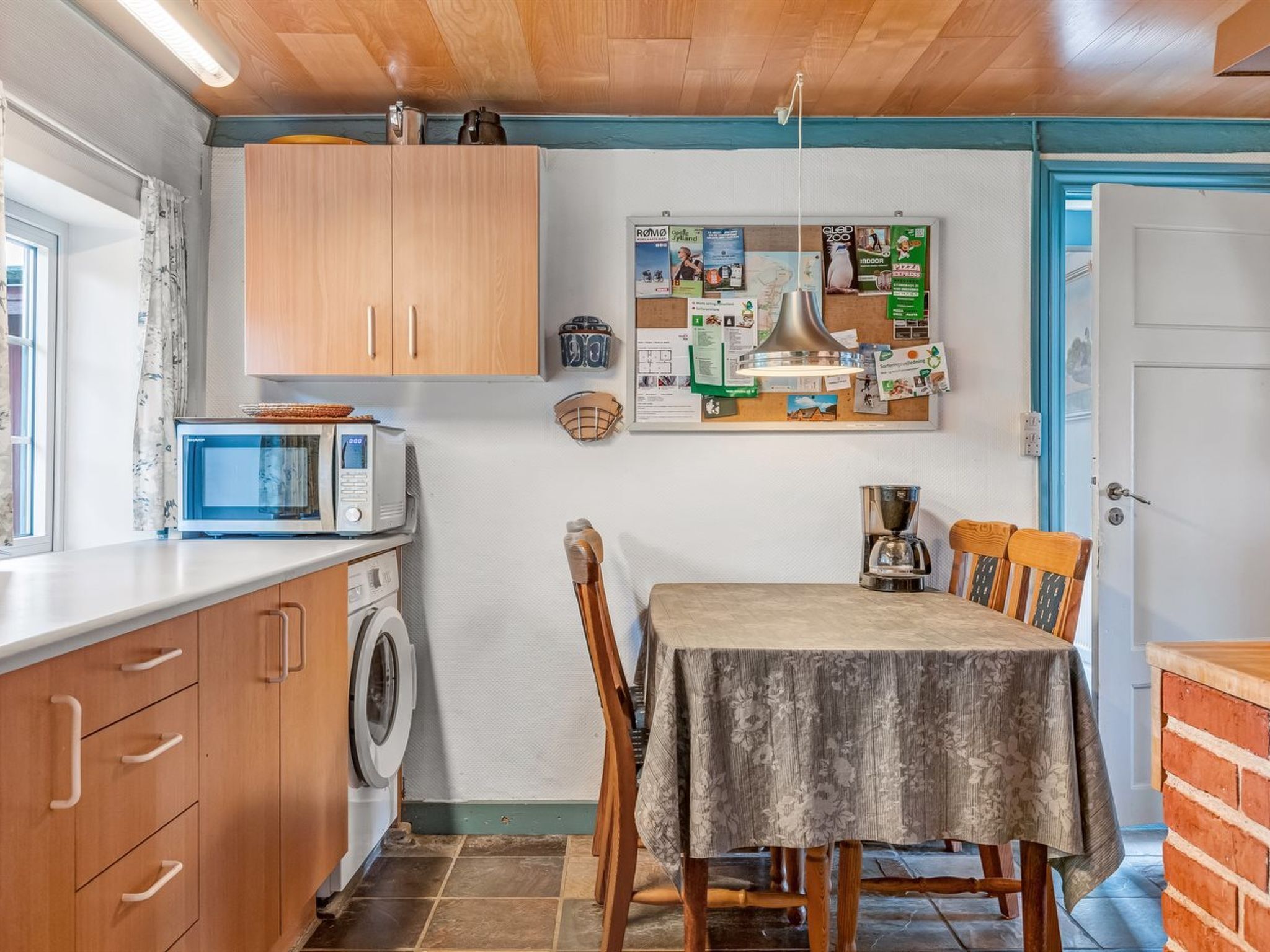 Ett kompakt kök med träskåp, en mikrovågsugn, en tvättmaskin och ett matbord med stolar.
