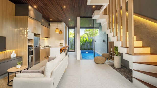 A modern kitchen with built-in appliances, a dining area with a white sofa, and a staircase leading to a balcony with a view of greenery. - Private Pool Vila 8B Close Melasti Beach (Ungasan)