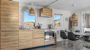 Una cocina moderna con armarios de madera, horno empotrado y comedor con sillas negras y una mesa.