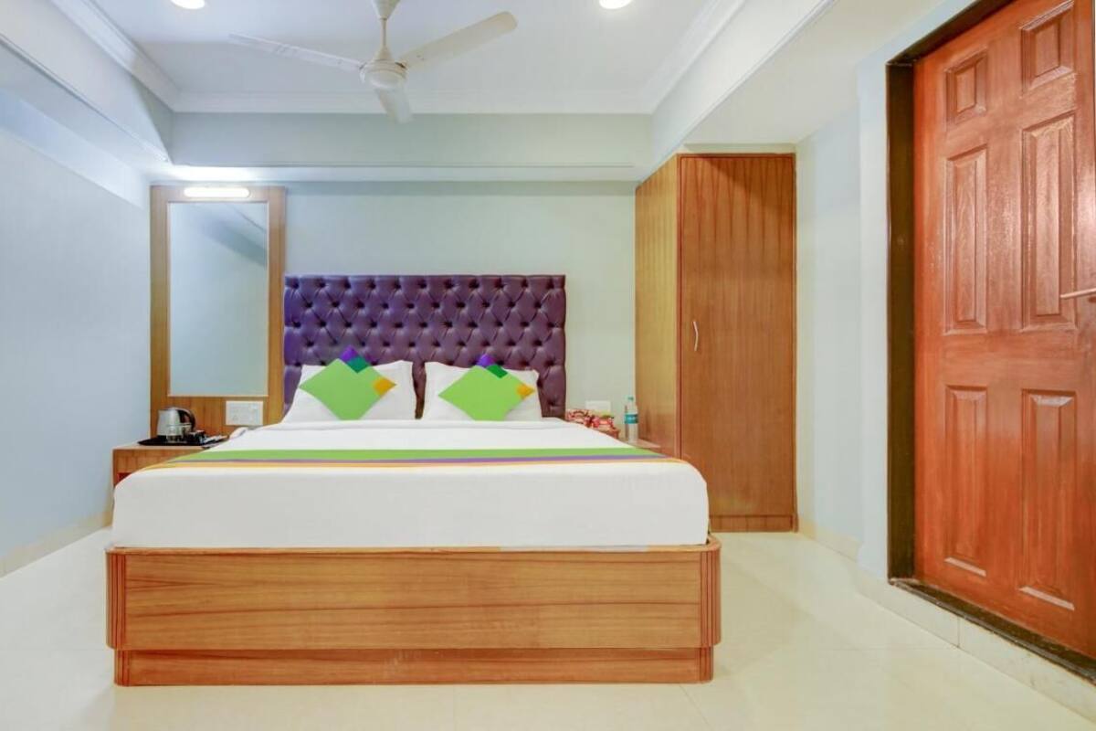 A bedroom with a tufted headboard, a bed with white bedding and green pillows, a nightstand with a lamp, and a wooden wardrobe.