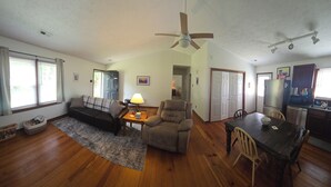 Ein geräumiges Wohnzimmer mit Sofa, Sessel, Esstisch und Deckenventilator.