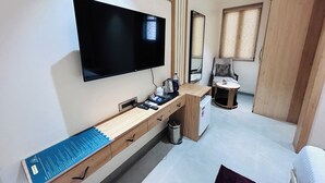 A modern hotel room with a flat-screen TV, wooden console, and a small round table with a chair. - HOTEL MEENA AURUM INN (Darbhanga)