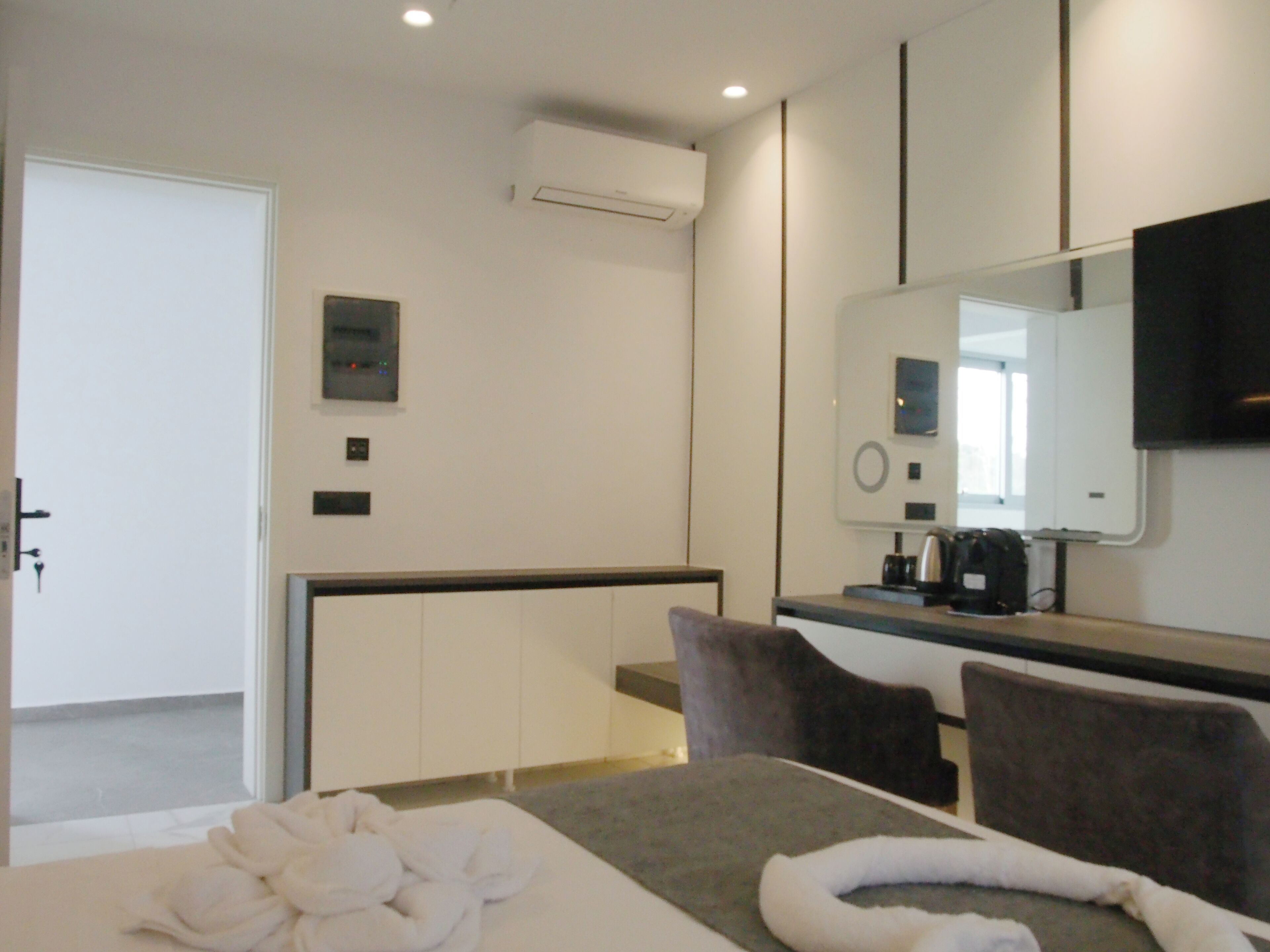 A modern hotel room with a bed, a desk with a coffee maker, a mirror, and a door.