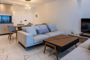 A modern living room with a sofa, coffee table, TV, and dining area. - Oros Paradise Hotel (Rhodes)