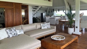 Ein modernes Wohnzimmer mit Ecksofa, Holztisch und Essbereich, im Hintergrund eine Küche.
