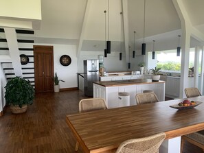 A modern kitchen with a central island, white cabinetry, and hanging pendant lights. - Angel Bay by Triang Villas - Nazaré  (Tabanan)