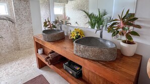 Ein Badezimmer mit einem SteinklopfZiegelbecken, einem Holzausziehtisch und einem großen Spiegel.
