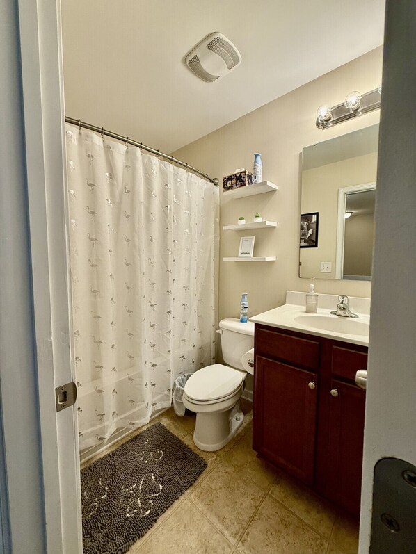 A bathroom with a toilet, a shower curtain, a sink, and a mirror.
