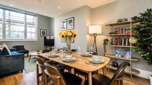 A dining area with a wooden table set for six, surrounded by black chairs. There is a bookshelf with books and decorative items, and a large window providing natural light. - Host Stay Catharine Quarters (Liverpool)