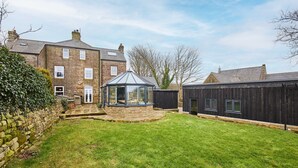 A stone house with a glass conservatory, a stone wall, and a grassy yard. - Host Stay The Churchside Well (Scarborough)