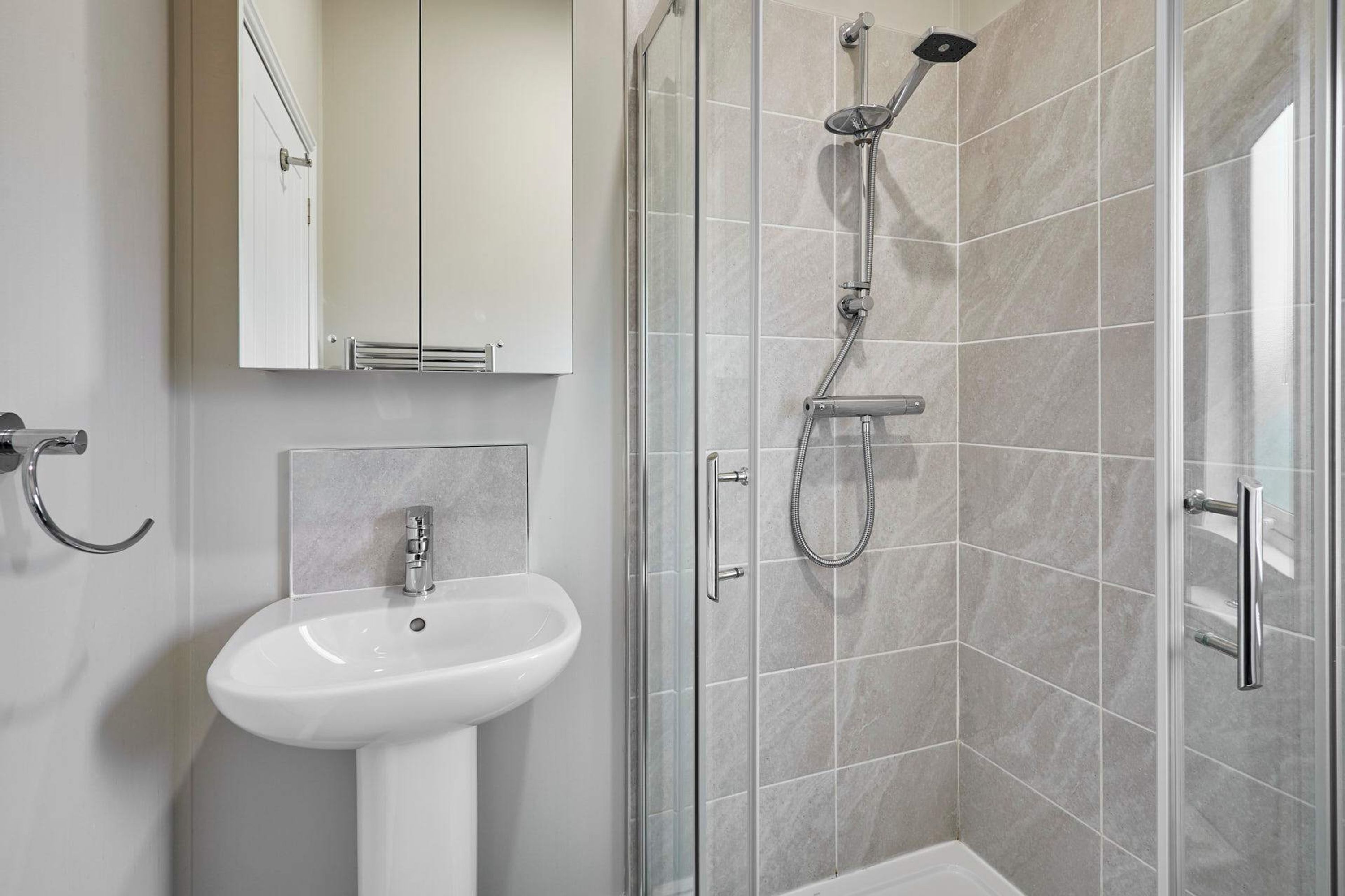 A modern bathroom with a glass-enclosed shower, a white pedestal sink, and a mirror above the sink.
