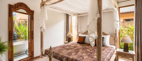 A room with a four-poster bed, a large mirror, and a small table with a decorative item.