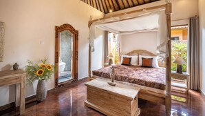 A spacious bedroom with a four-poster bed, a wooden nightstand, a vase with sunflowers, and a large mirror. - Genie Private Villa by Travellink Bali (Ubud)