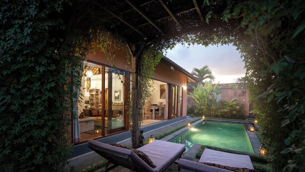 A serene outdoor pool area with lounge chairs and a well-lit interior space visible through glass doors. - Genie Private Villa by Travellink Bali (Ubud)
