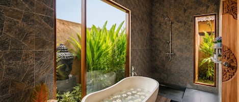Un baño moderno con una bañera independiente, una ducha y un ventanal con vistas a la vegetación.