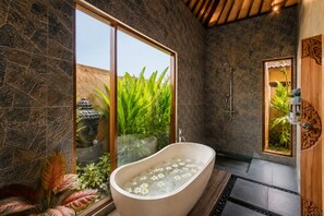 Ein modernes Badezimmer mit einer freistehenden Badewanne, einer Dusche und einem großen Fenster mit Blick auf Grünflächen.