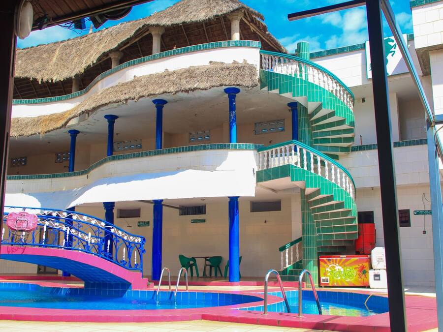 Un hotel con zona de piscina, una escalera y una estructura con techo de paja.