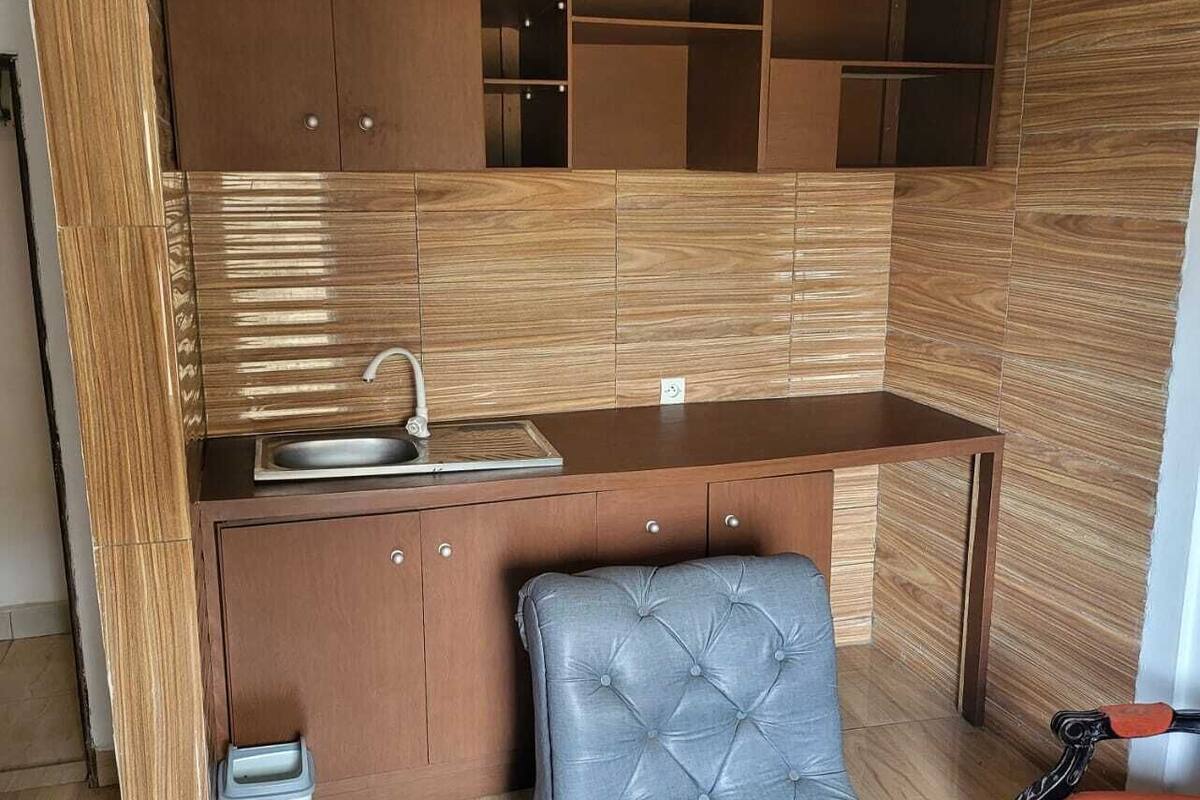 Una cocina compacta con armarios de madera, un lavamanos empotrado y una pequeña zona de estar con una butaca tapizada y una mesa.