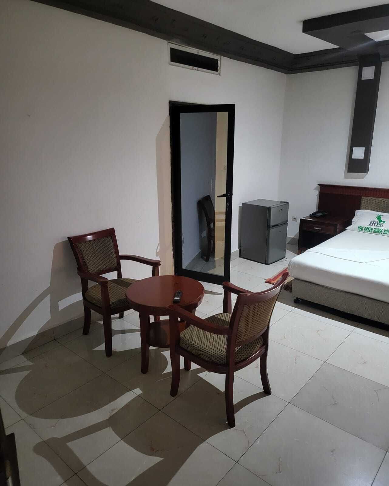 A hotel room with a bed, a desk, two chairs, a small table, a mirror, and a wardrobe.