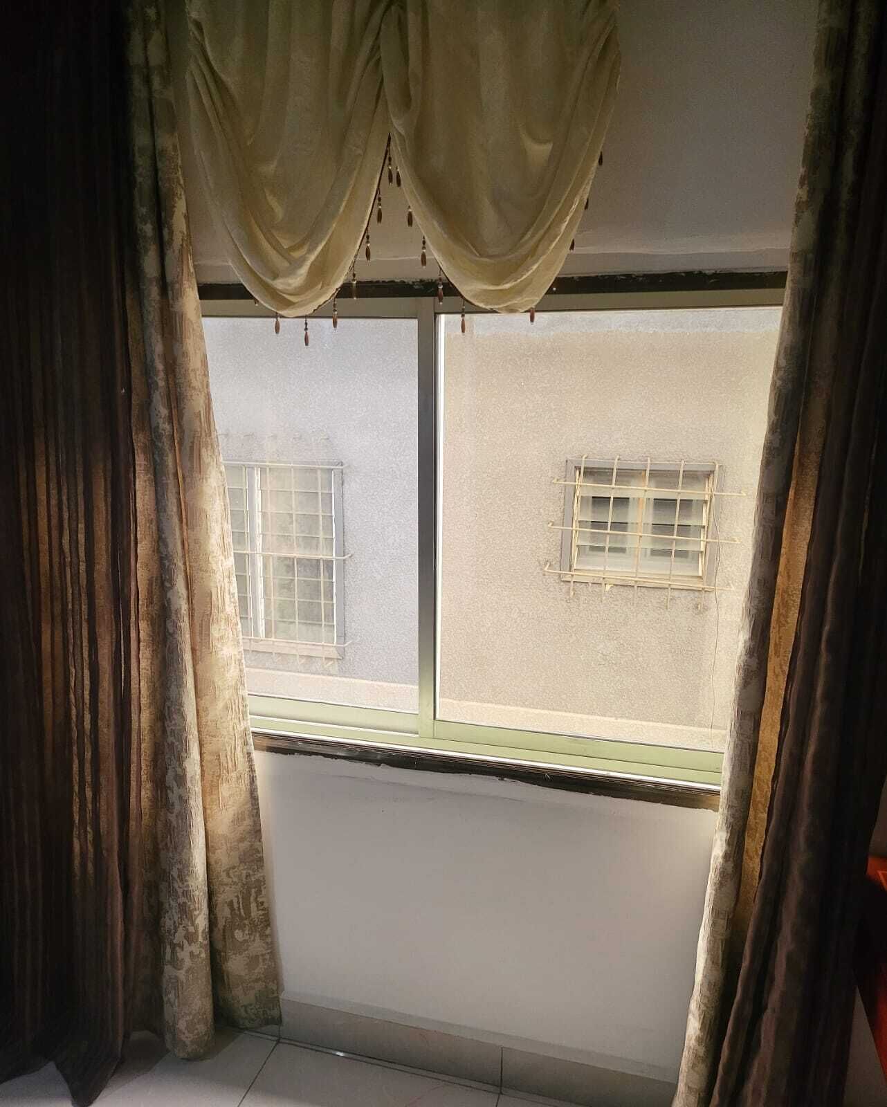 A room with a large window, curtains, and a view of a building outside.