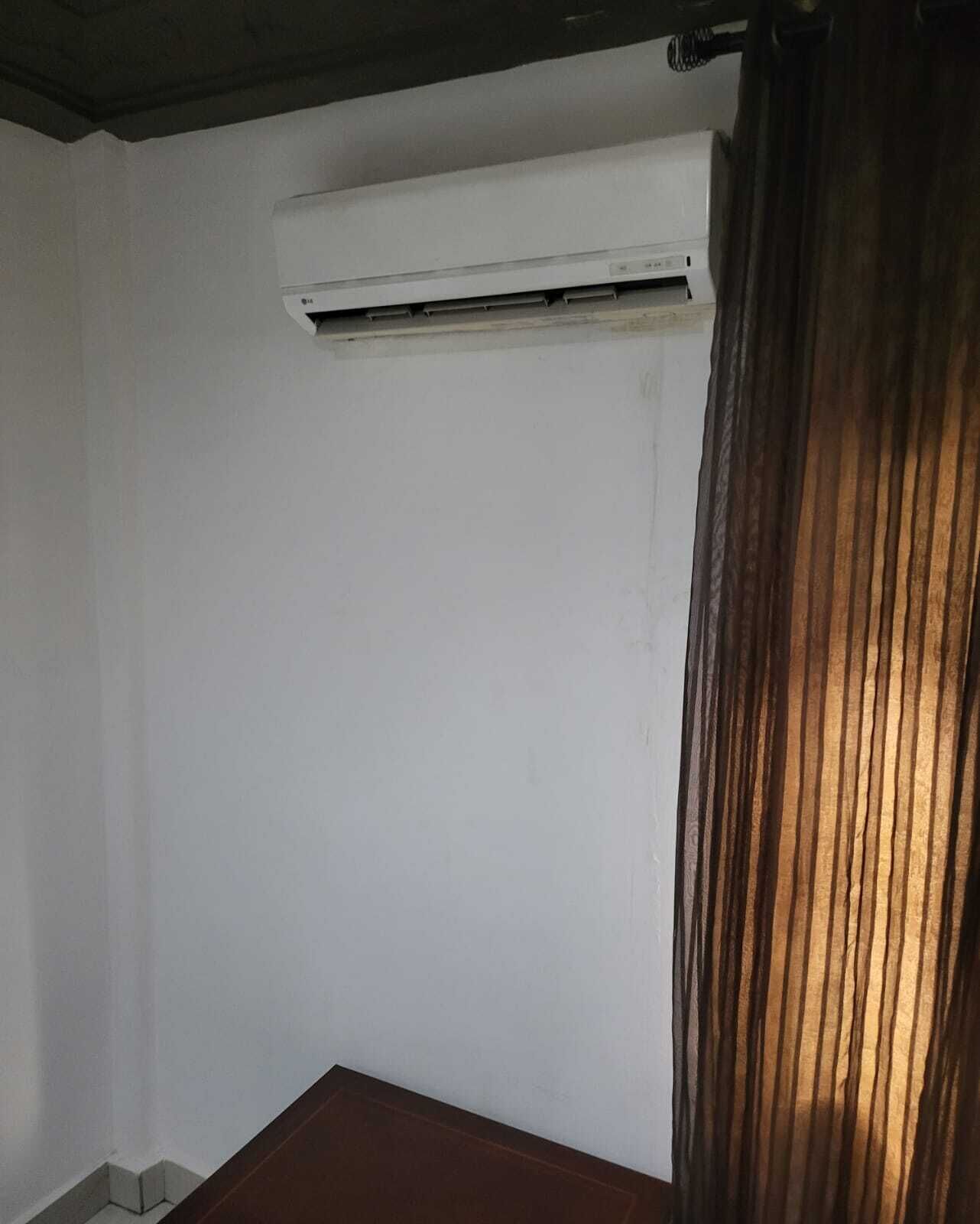 A room with a white wall, a wooden table, and a window with a curtain.