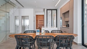 A modern dining area with a wooden table and wicker chairs, a glass wall, and a wooden door. - Periyiali Resort - Front Line Villa 08 Chronos (Paralimni)