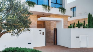 A modern building with a stone facade, a wooden door, and a white entrance. - Periyiali Resort - Front Line Villa 08 Chronos (Paralimni)