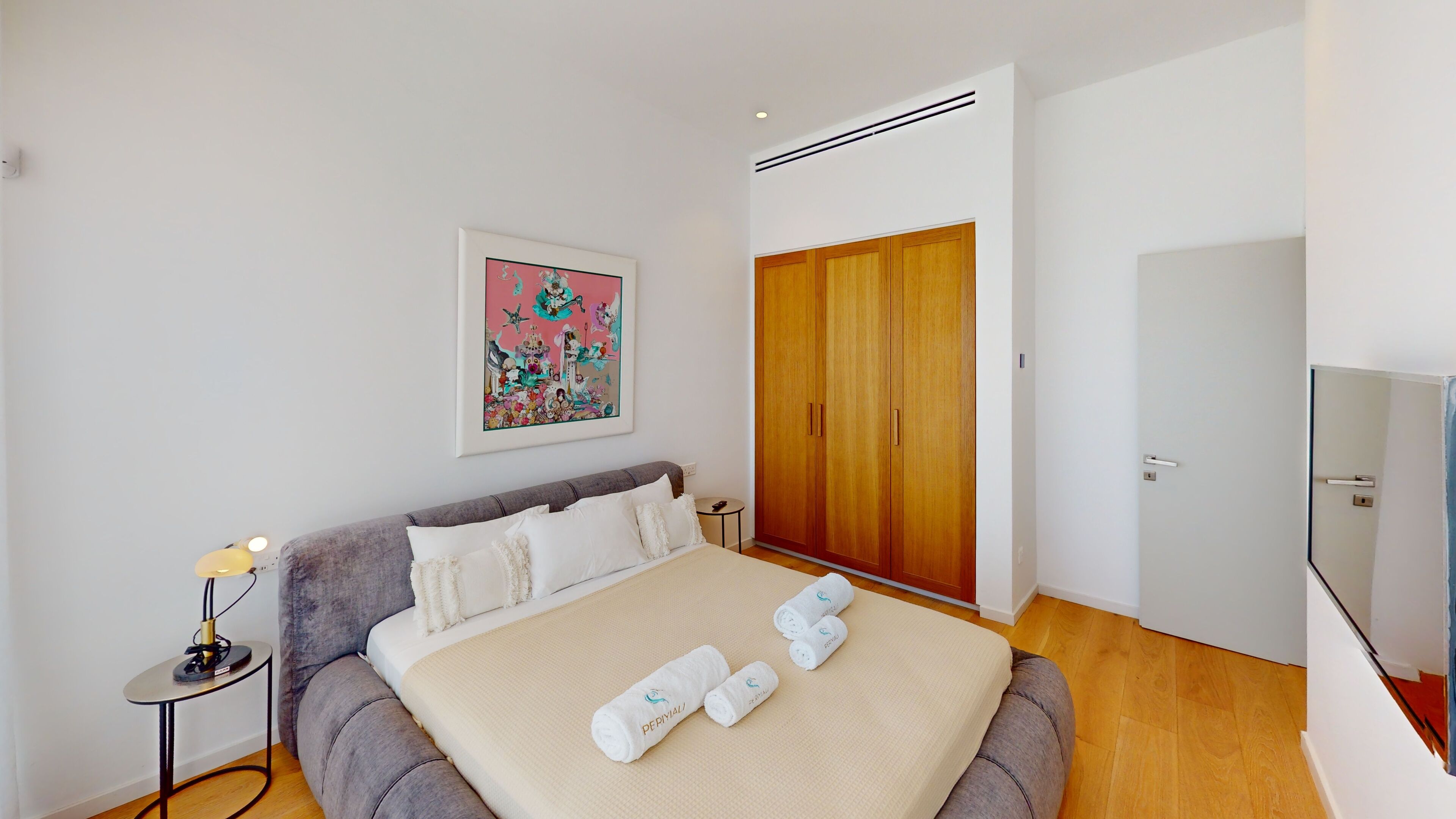 A neatly arranged bedroom with a bed, a bedside table with a lamp, a wardrobe, and a framed picture on the wall.