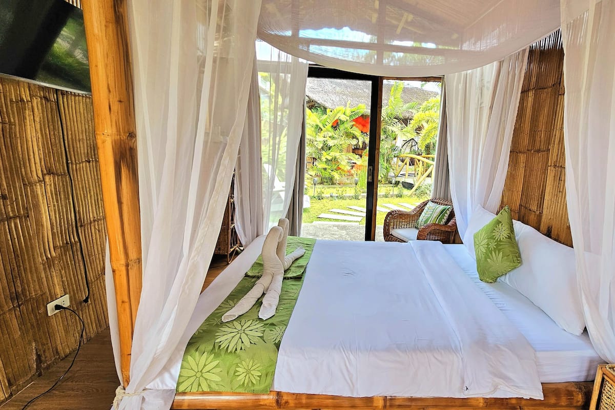 A bed with a canopy, a green patterned bedspread, and a single green pillow.
