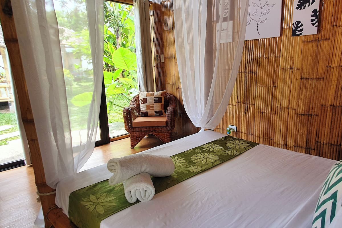 A room with a bed, a chair, and a view of greenery outside.