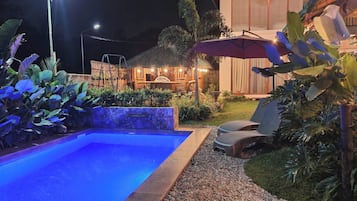 Relax by the pool surrounded by lush tropical plants and a thatched-roof patio.