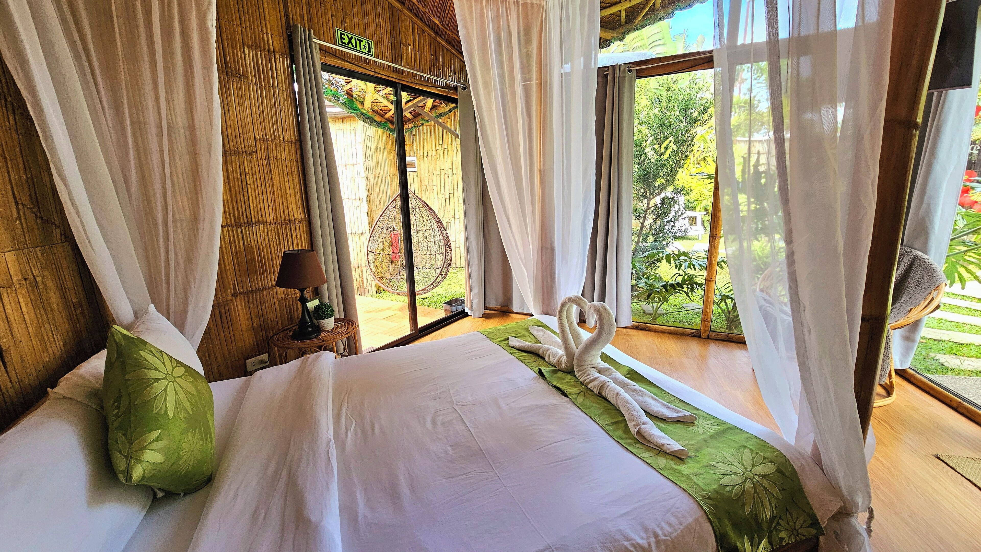 Una habitación con una cama, una almohada verde, una lámpara y vistas al exterior con vegetación.