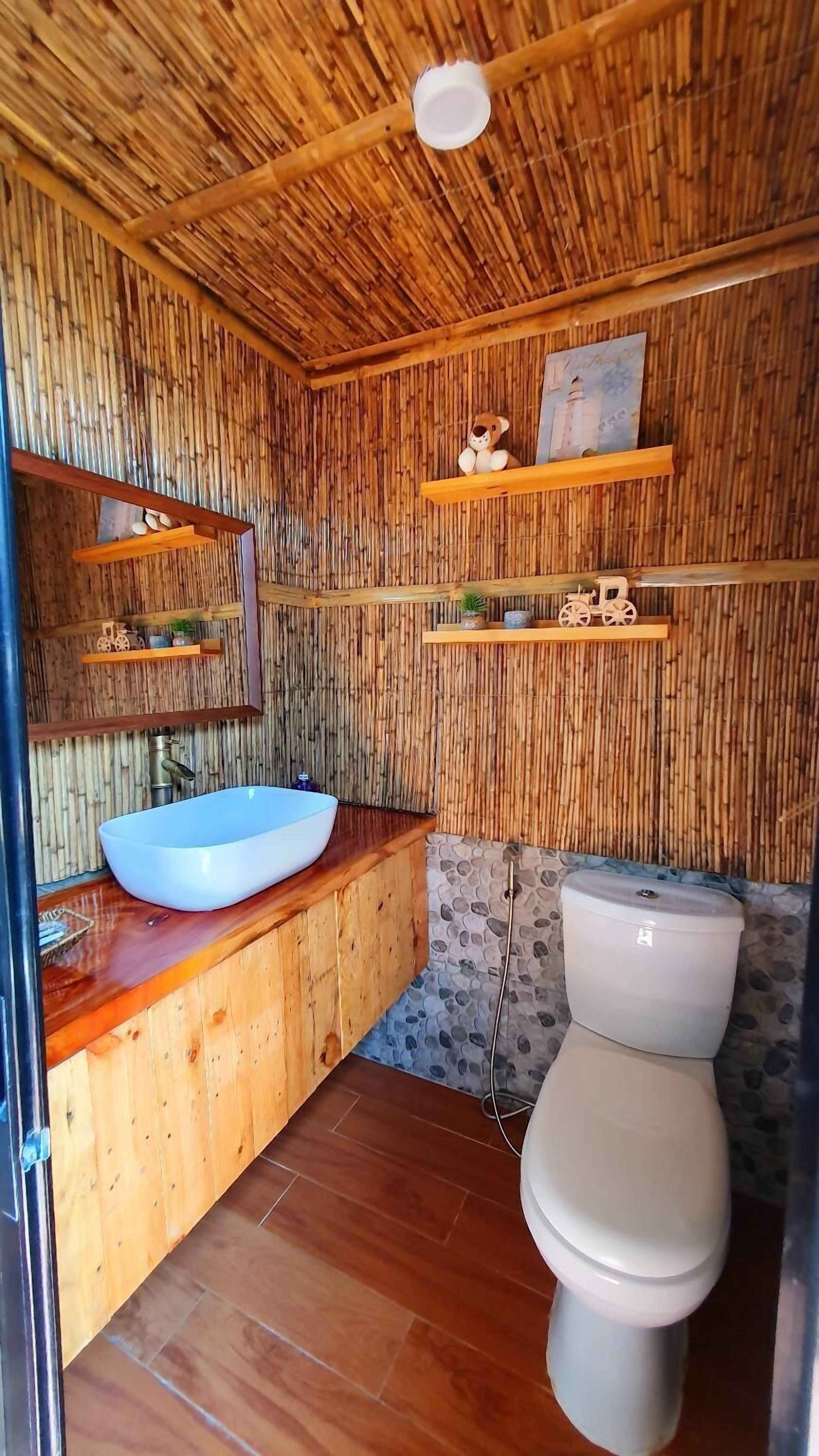 A bathroom with a bamboo wall, a wooden vanity, a white sink, a toilet, and shelves with decorative items.