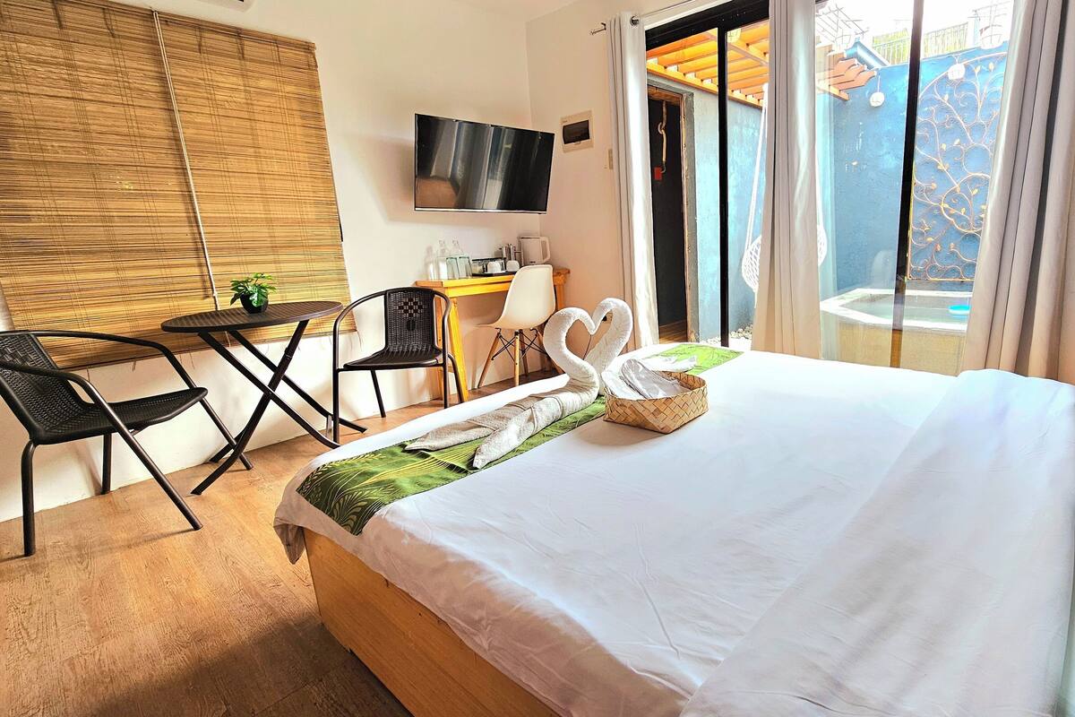 A hotel room with a bed, a desk, a chair, a TV, and a view of the outside.